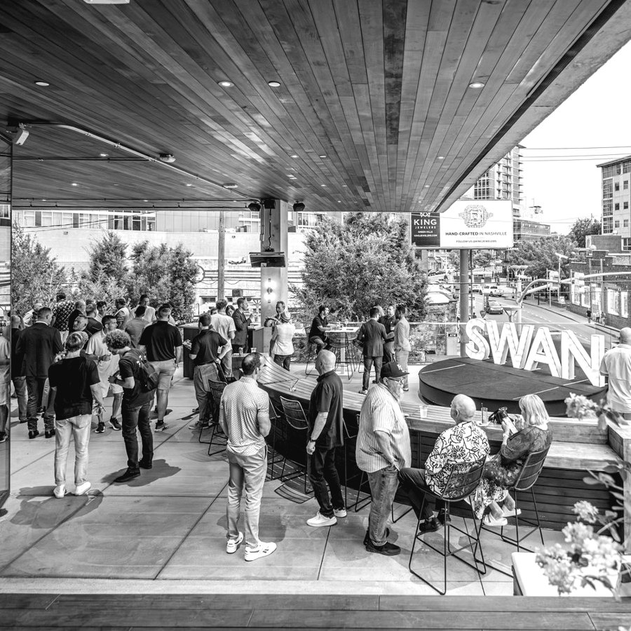 A crowded rooftop bar event with a large Swan sign.