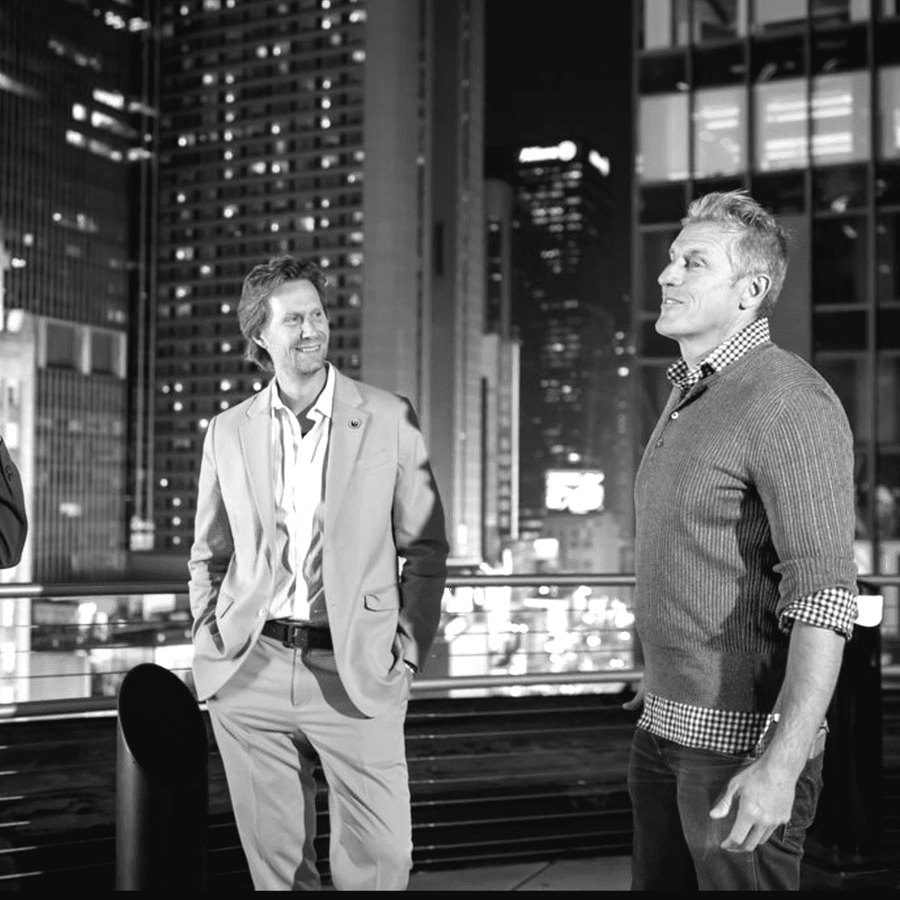 Two guests talking at a rooftop reception at night, city towers behind them.